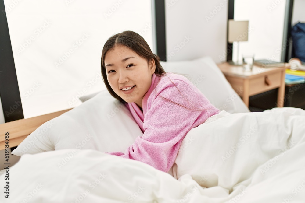 ¡Young chinese girl smiling happy and hugging pillow lying on the bed at bedroom.