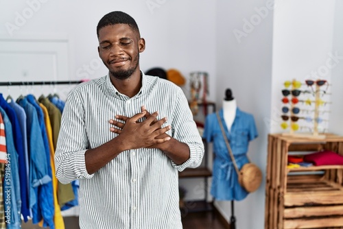 Young african american man working as manager at retail boutique smiling with hands on chest with closed eyes and grateful gesture on face. health concept.