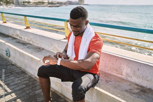 Young african american man wearing sportswear looking watch at seaside