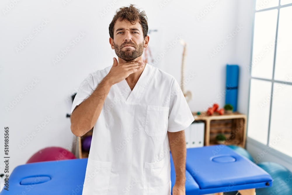 Young handsome physiotherapist man working at pain recovery clinic cutting throat with hand as knife, threaten aggression with furious violence Young handsome physiotherapist man working at pain recovery clinic cutting throat with hand as knife, threaten aggression with furious violence