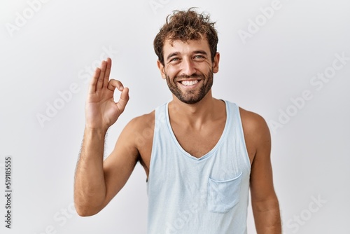 Young handsome man standing over isolated background smiling positive doing ok sign with hand and fingers. successful expression.