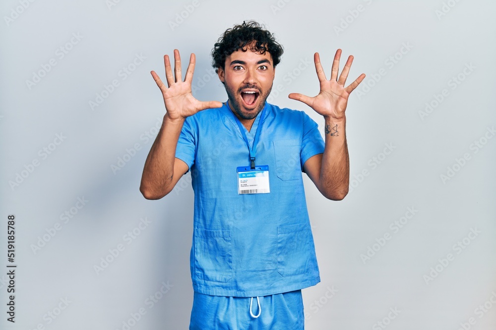 Young hispanic man wearing blue male nurse uniform celebrating crazy and amazed for success with arms raised and open eyes screaming excited. winner concept Young hispanic man wearing blue male nurse uniform celebrating crazy and amazed for success with arms raised and open eyes screaming excited. winner concept