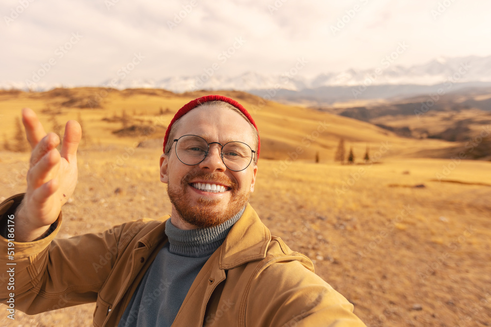 Concept Adventure Traveler with backpack. Hipster man in glasses and red hat takes selfie photo background autumn mountains Altai Concept Adventure Traveler with backpack. Hipster man in glasses and red hat takes selfie photo background autumn mountains Altai