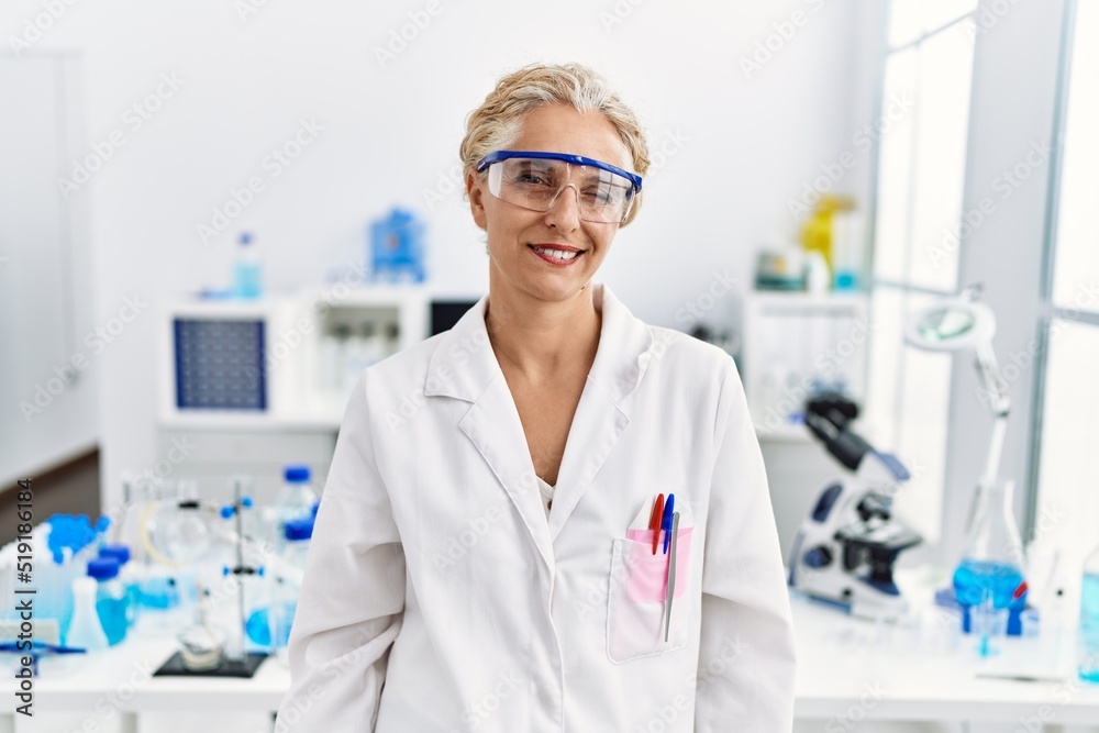 Middle age blonde woman working at scientist laboratory winking looking at the camera with sexy expression, cheerful and happy face. Middle age blonde woman working at scientist laboratory winking looking at the camera with sexy expression, cheerful and happy face.