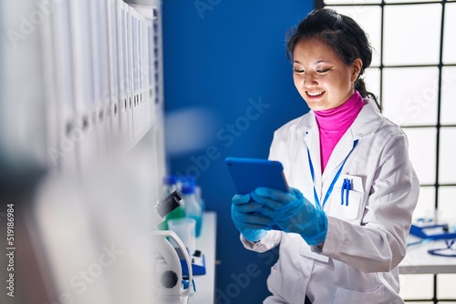 Young chinese woman scientist smiling confident using touchpad at laboratory