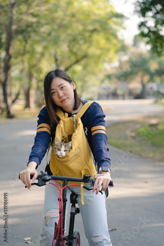 asian woman biking bicycle with her cat in backpack at park