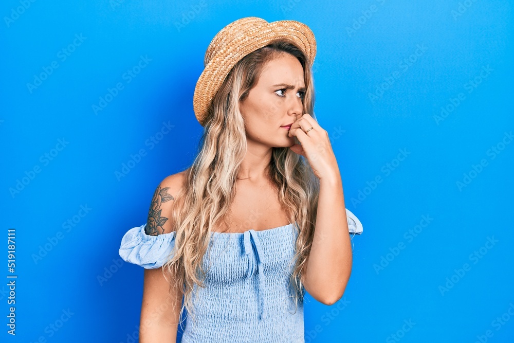 Beautiful young blonde woman wearing summer hat looking stressed and nervous with hands on mouth biting nails. anxiety problem. Beautiful young blonde woman wearing summer hat looking stressed and nervous with hands on mouth biting nails. anxiety problem.