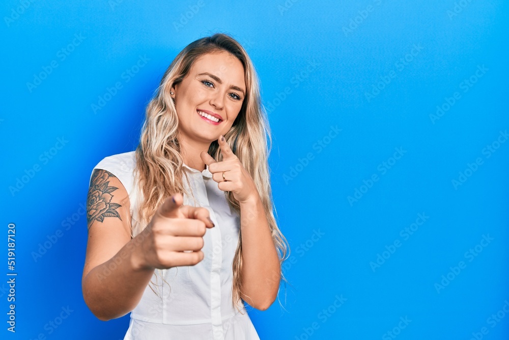 Beautiful young blonde woman wearing casual white shirt pointing fingers to camera with happy and funny face. good energy and vibes. Beautiful young blonde woman wearing casual white shirt pointing fingers to camera with happy and funny face. good energy and vibes.