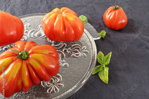 Close up of awesome ripe slicing tomatoes placed on a decorative glass plate. Dark tablecloth. Different forms. 