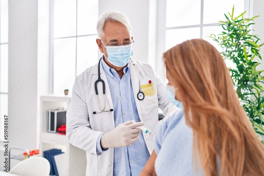 Middle age man and woman doctor wearing medical mask vaccinating patient at clinic Middle age man and woman doctor wearing medical mask vaccinating patient at clinic