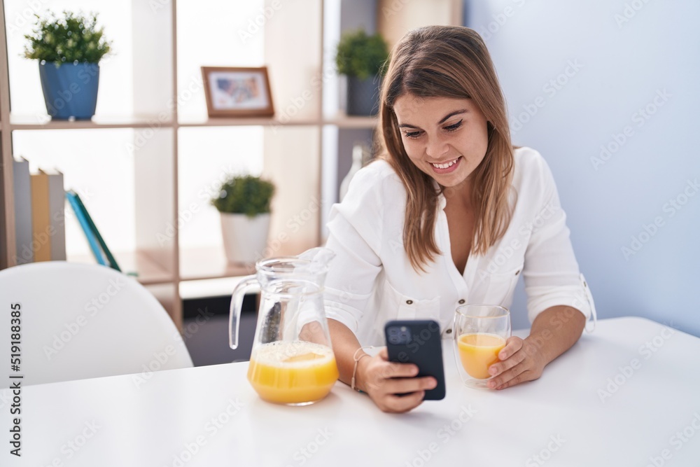 Young woman using smartphone drinking orange juice at home
