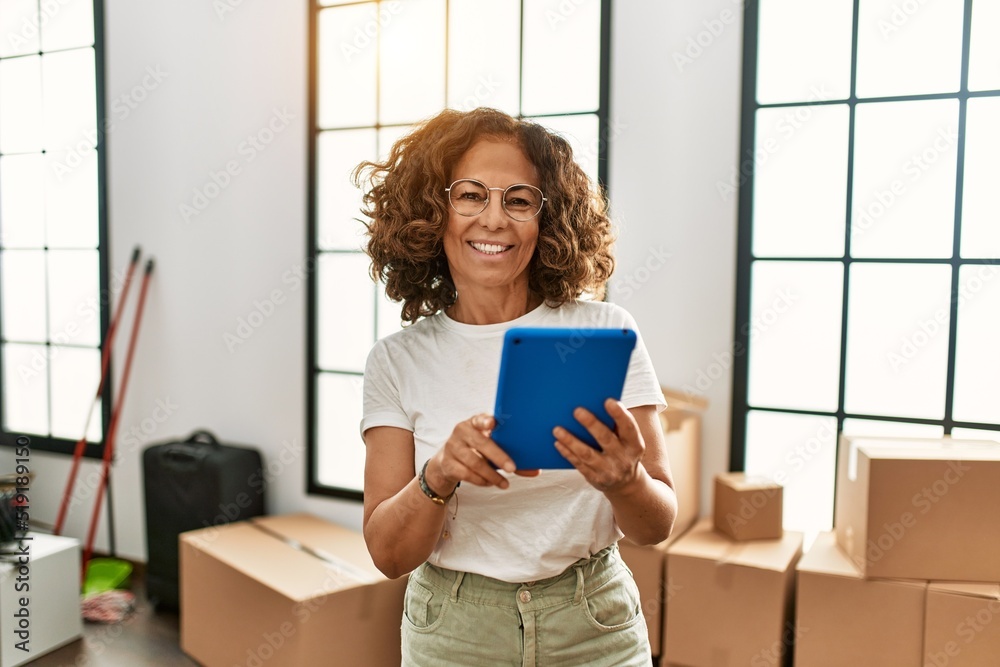 Middle age hispanic woman smiling confident using touchpad at new home Middle age hispanic woman smiling confident using touchpad at new home