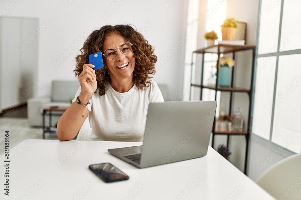 Middle age hispanic woman using laptop holding credit card at home Middle age hispanic woman using laptop holding credit card at home