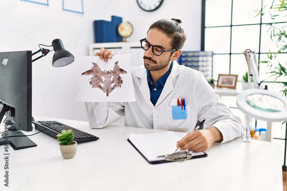 Handsome hispanic man working as psychologist showing rorschach test at professional clinic