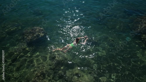 4k slowmotion top view sexy slim woman with nise buttocks in green swimsuit floating in clear turquoise water of mediterranean sea close to shore. vacation and wellness, Summer Season Fethiye, Turkey photo