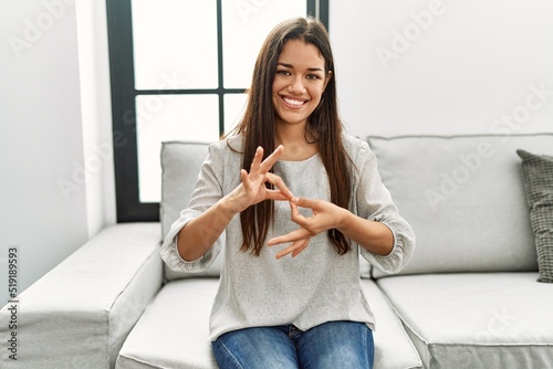 Young latin woman talking with sign language sitting on sofa at home photo