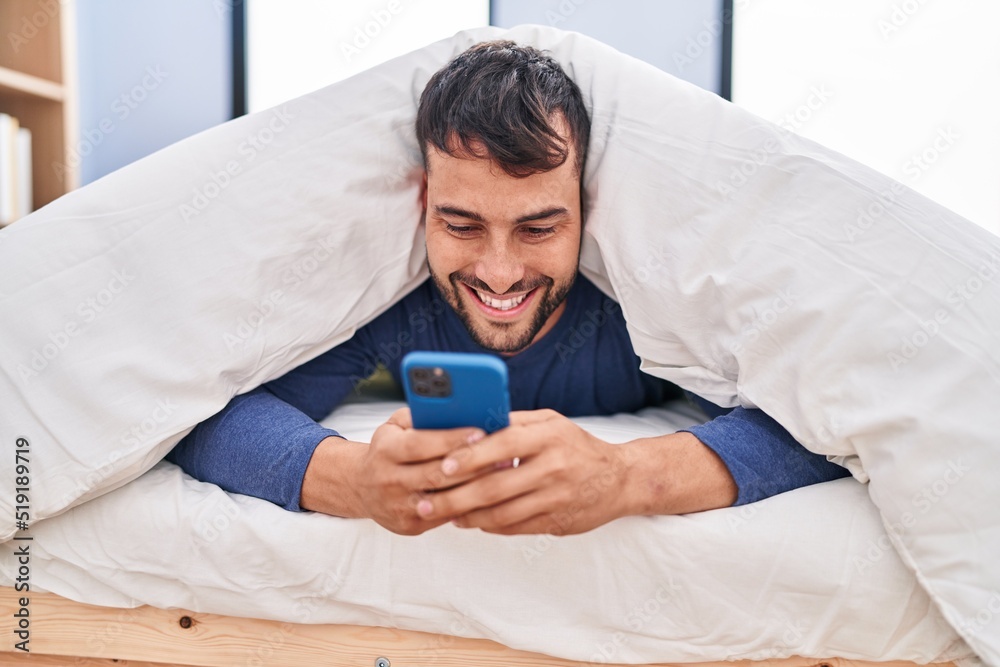 Young hispanic man using smartphone lying on bed at bedroom Young hispanic man using smartphone lying on bed at bedroom