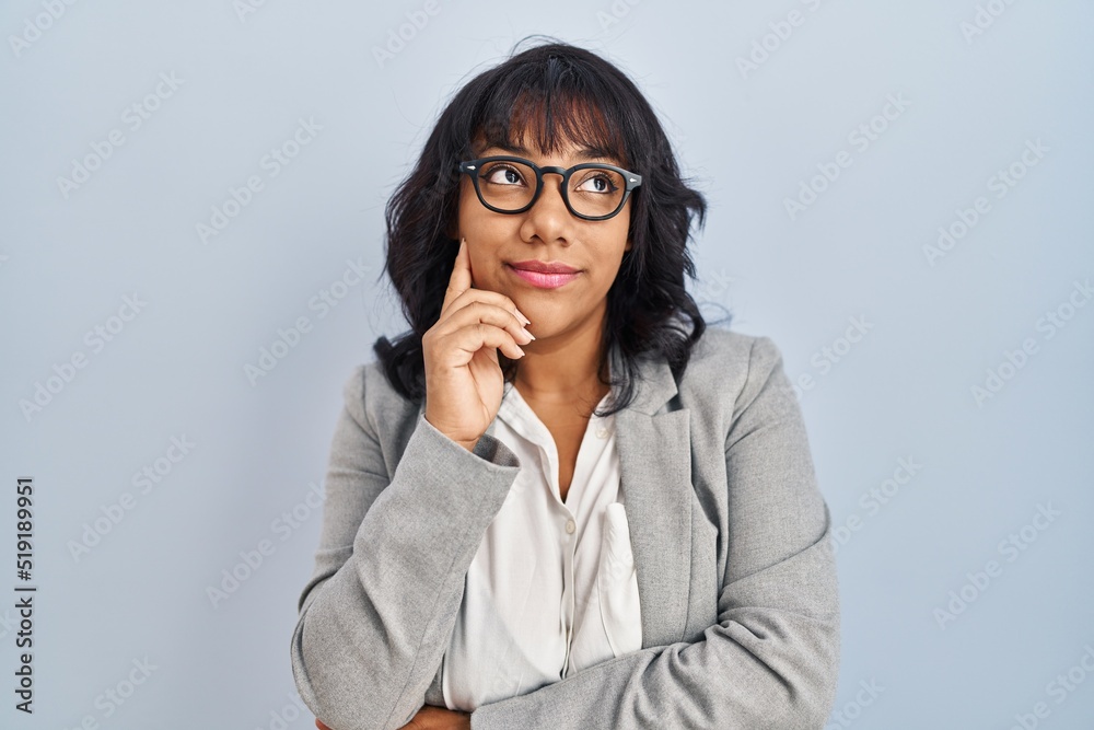 Hispanic woman standing over isolated background with hand on chin thinking about question, pensive expression. smiling with thoughtful face. doubt concept.