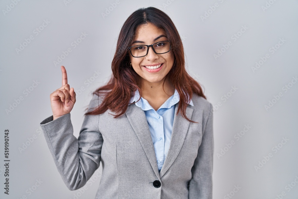 Hispanic young business woman wearing glasses showing and pointing up with finger number one while smiling confident and happy. Hispanic young business woman wearing glasses showing and pointing up with finger number one while smiling confident and happy.