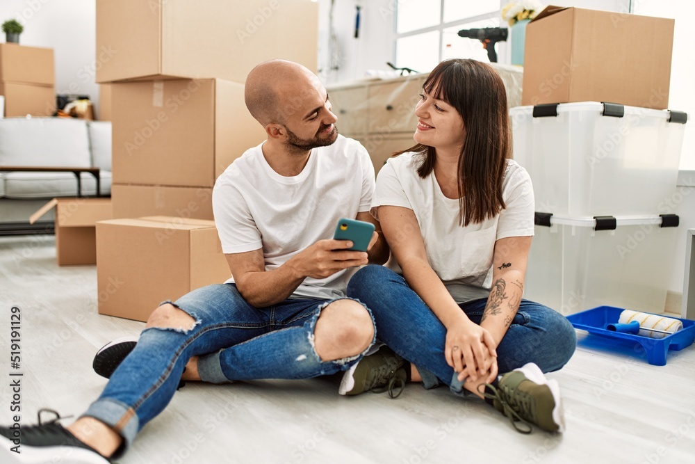 Young hispanic couple smiling happy using smartphone at new home. Young hispanic couple smiling happy using smartphone at new home.