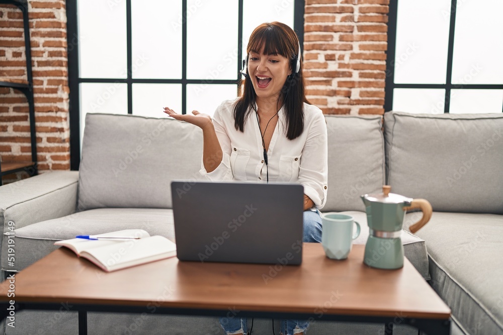 Young brunette woman working from home wearing operator headset celebrating achievement with happy smile and winner expression with raised hand Young brunette woman working from home wearing operator headset celebrating achievement with happy smile and winner expression with raised hand
