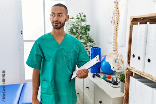 African american physiotherapist man working at pain recovery clinic smiling looking to the side and staring away thinking.