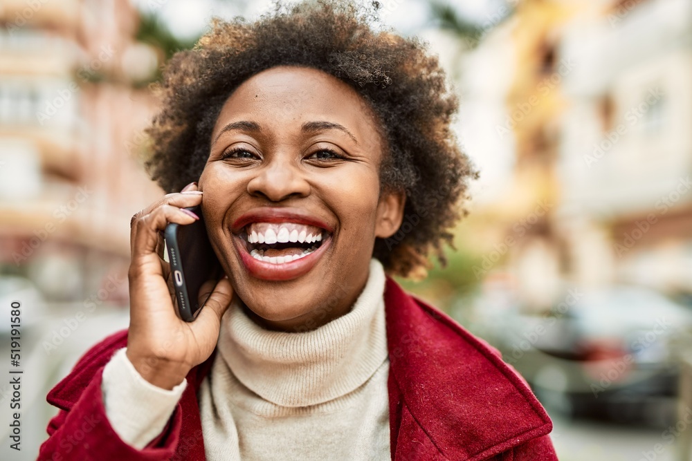 Beautiful business african american woman with afro hair smiling happy and confident outdoors at the city having a conversation speaking on the phone Beautiful business african american woman with afro hair smiling happy and confident outdoors at the city having a conversation speaking on the phone
