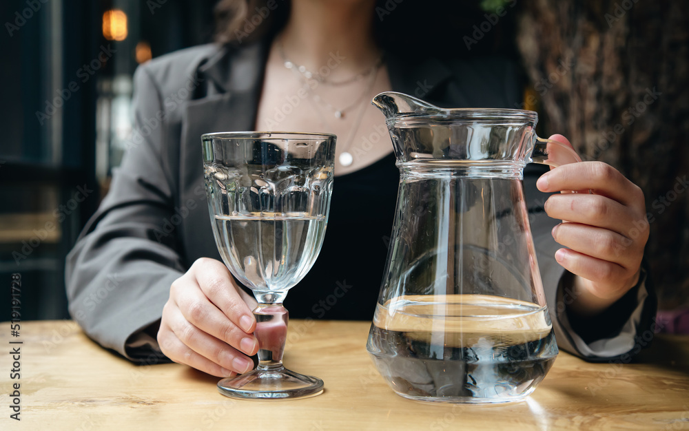 Close-up, a woman pours water into a glass in a cafe.