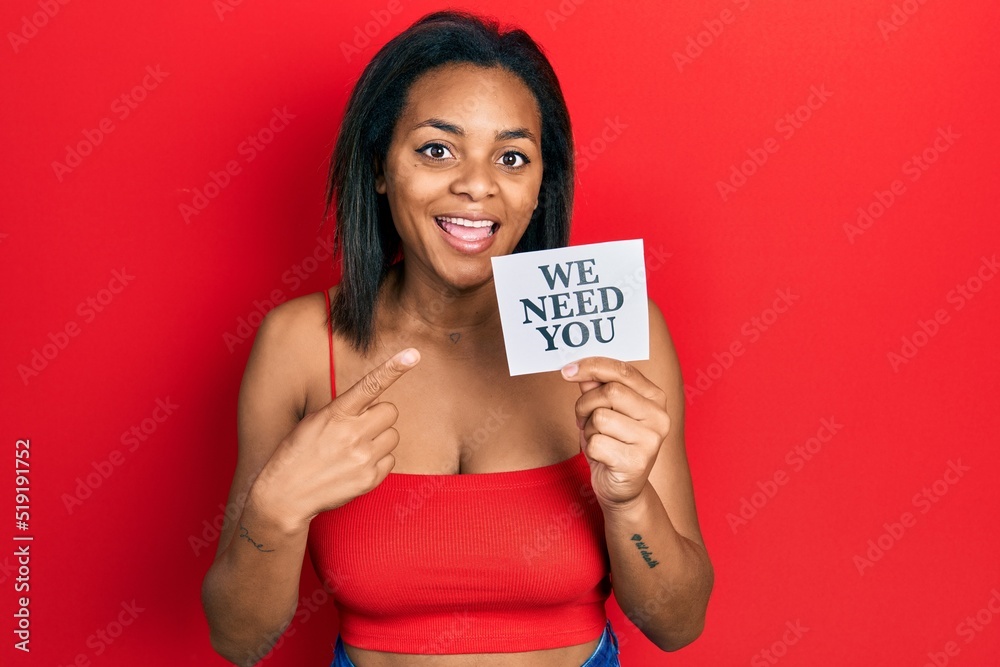 Young african american girl holding we need you paper smiling happy pointing with hand and finger Young african american girl holding we need you paper smiling happy pointing with hand and finger