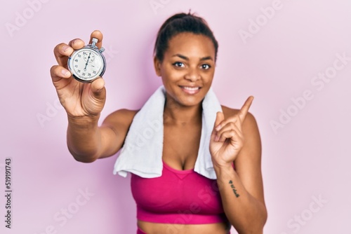 Young african american girl wearing sportswear holding stopwatch smiling happy pointing with hand and finger to the side