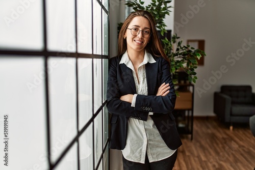 Young hispanic woman business worker standing with arms crossed gesture at office