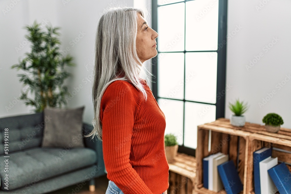 Middle age grey-haired woman wearing casual clothes standing at home looking to side, relax profile pose with natural face with confident smile. Middle age grey-haired woman wearing casual clothes standing at home looking to side, relax profile pose with natural face with confident smile.