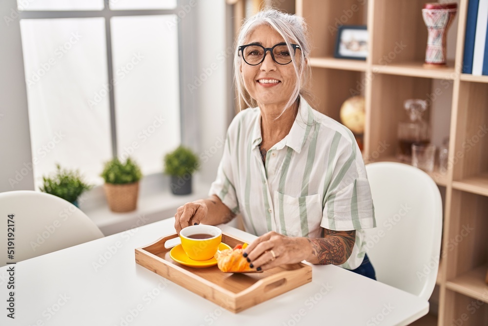 Middle age grey-haired woman having breakfast sitting on table at home Middle age grey-haired woman having breakfast sitting on table at home