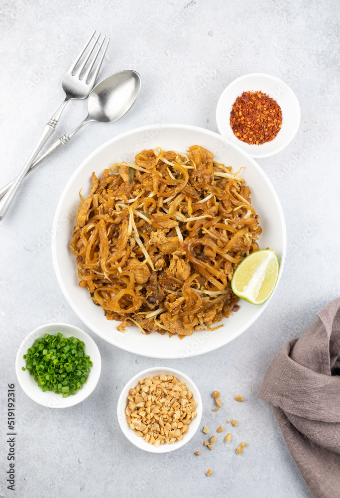 Pad thai with chicken, dried chili, peanuts, lime and green onions on a gray background, top view. Thai fried noodles with vegetables, tofu, nuts, chicken and spices. Pad thai with chicken, dried chili, peanuts, lime and green onions on a gray background, top view. Thai fried noodles with vegetables, tofu, nuts, chicken and spices.