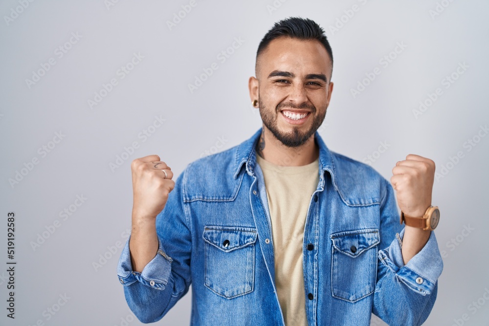 Young hispanic man standing over isolated background celebrating surprised and amazed for success with arms raised and eyes closed. winner concept. Young hispanic man standing over isolated background celebrating surprised and amazed for success with arms raised and eyes closed. winner concept.