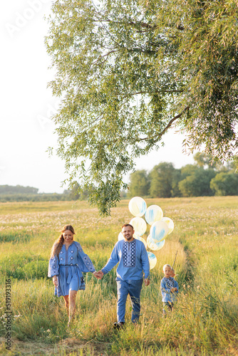 Happy parents with two their twins sons walk on meadow with air balloons in their hands. © Stanislav