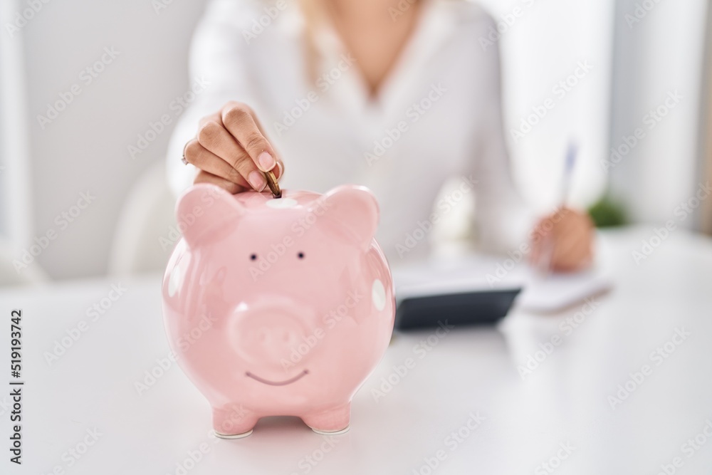 Young woman inserting coin on piggy bank at home - obrazy, fototapety, plakaty 