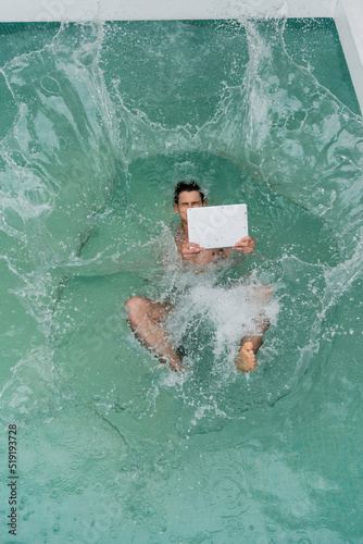 top view of freelancer with laptop falling in pool with turquoise water.