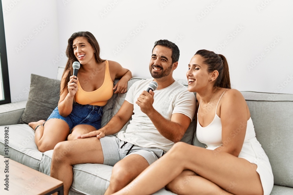 Three hispanic friends smiling happy singing song using microphone at home.
