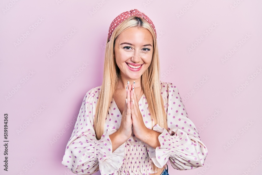 Young blonde girl wearing casual clothes praying with hands together asking for forgiveness smiling confident.