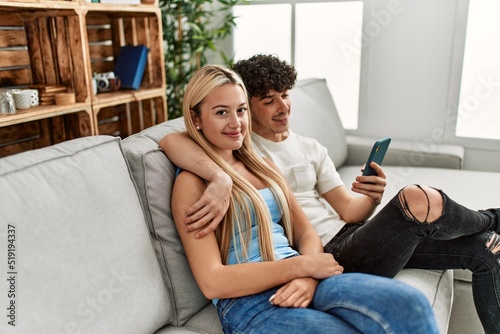 Young couple using smartphone sitting on the sofa at home.