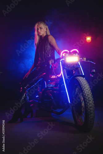 Young beautiful girl in the neon lights stands near the motorbike.