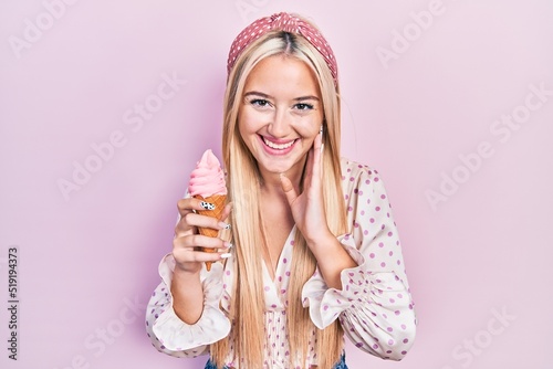 Young blonde girl holding ice cream smiling and laughing hard out loud because funny crazy joke.
