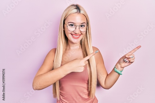 Young blonde girl wearing casual clothes smiling and looking at the camera pointing with two hands and fingers to the side.