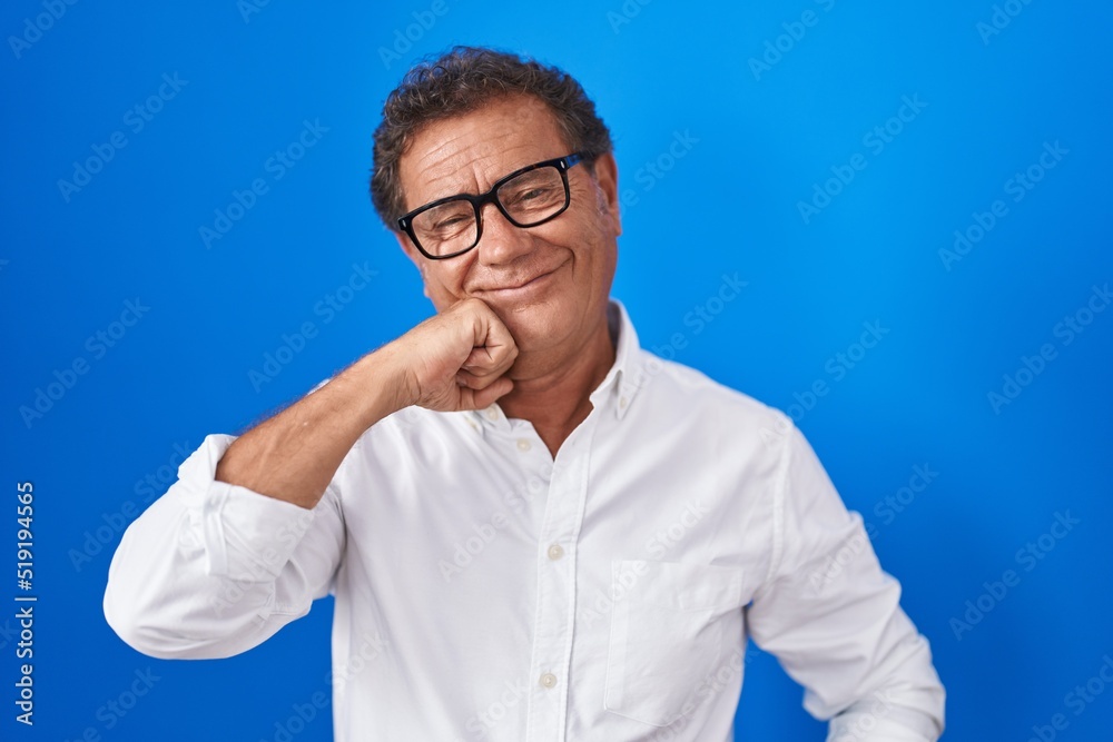 Middle age hispanic man standing over blue background with hand on chin thinking about question, pensive expression. smiling with thoughtful face. doubt concept. Middle age hispanic man standing over blue background with hand on chin thinking about question, pensive expression. smiling with thoughtful face. doubt concept.