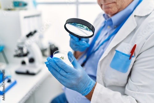 Middle age grey-haired man wearing scientist uniform using loupe at laboratory