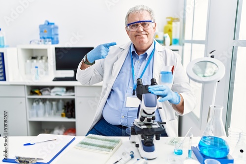 Senior caucasian man working at scientist laboratory smiling cheerful showing and pointing with fingers teeth and mouth. dental health concept.