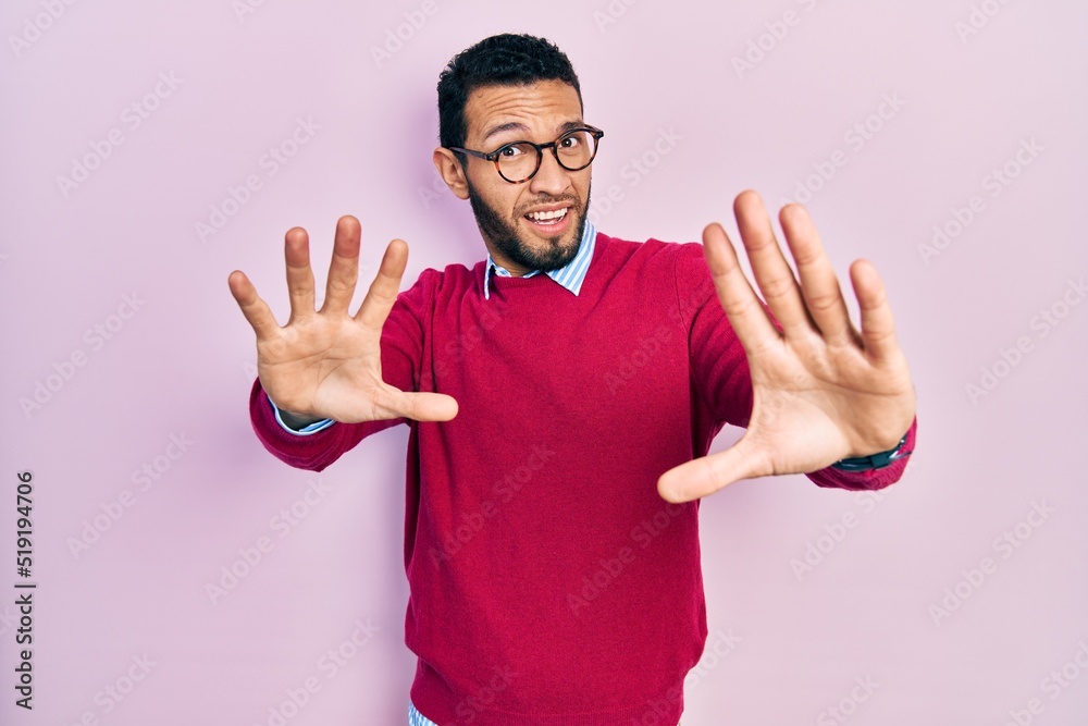 Hispanic man with beard wearing business shirt and glasses afraid and terrified with fear expression stop gesture with hands, shouting in shock. panic concept. Hispanic man with beard wearing business shirt and glasses afraid and terrified with fear expression stop gesture with hands, shouting in shock. panic concept.