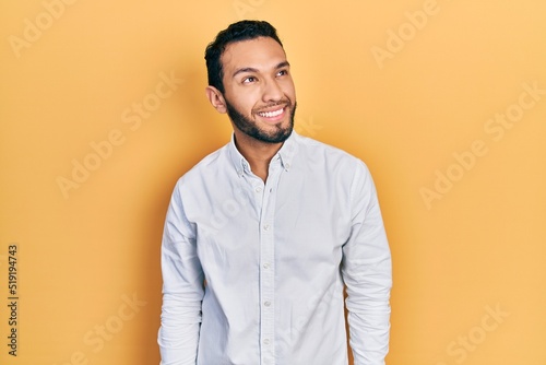Hispanic man with beard wearing business shirt looking away to side with smile on face, natural expression. laughing confident.