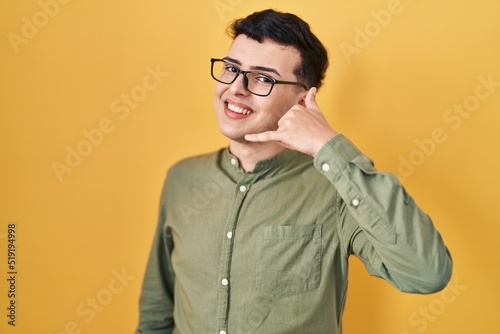 Non binary person standing over yellow background smiling doing phone gesture with hand and fingers like talking on the telephone. communicating concepts.
